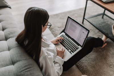 A student sat in front of a sofa using their laptop